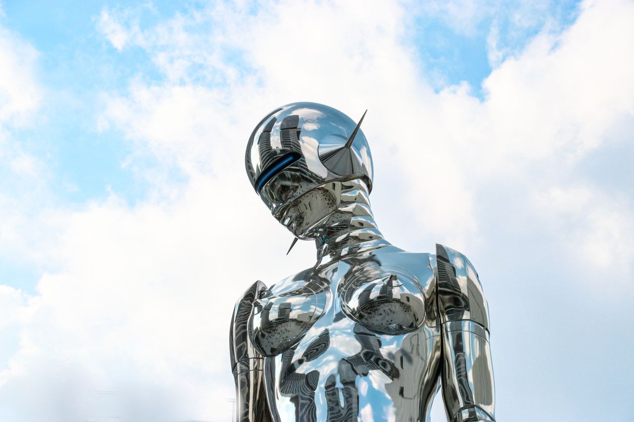 services-img A sleek chrome robot sculpture stands against a bright blue sky background.